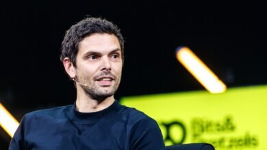 Man with dark hair and a microphone sits on stage.