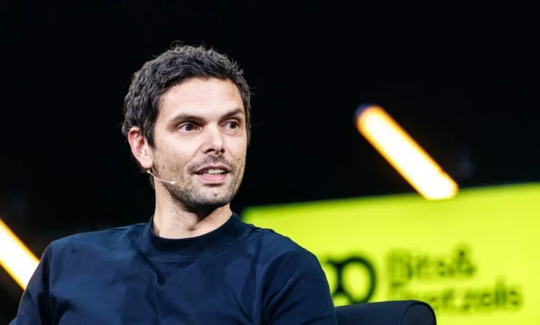 Man with dark hair and a microphone sits on stage.