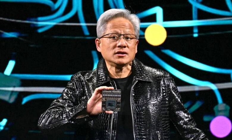 Jensen Huang holds a chip on stage, wearing a black jacket.