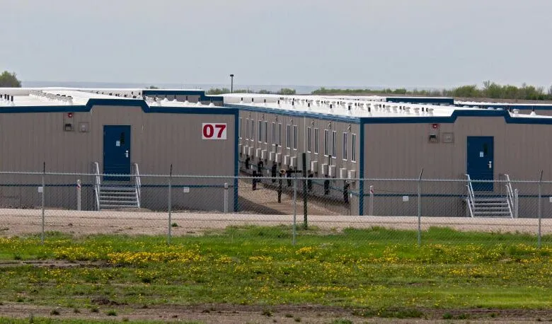 Modular housing units with numbered entrances behind a chain-link fence.