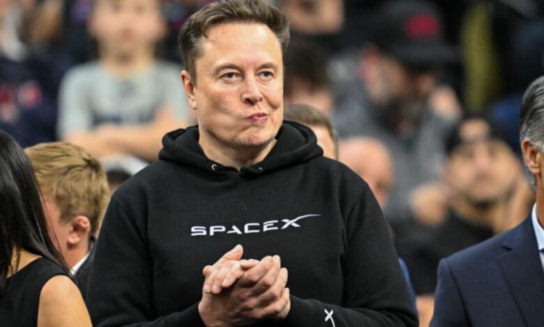 Elon Musk watches wrestling match wearing a SpaceX hoodie.