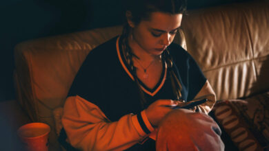 Teenage girl with braids sits on a couch, looking at her phone.