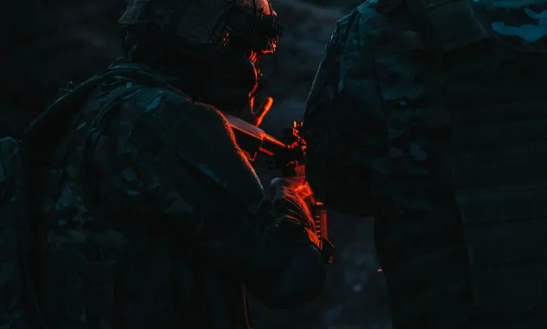 Two soldiers in camouflage gear aiming rifles in low light.
