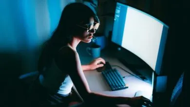 Woman with glasses works on computer in dark blue room.