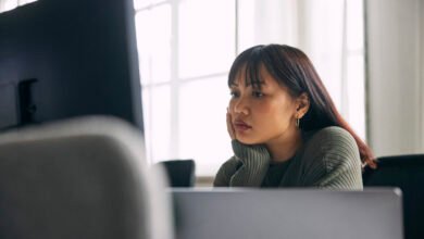 Woman with bangs rests her chin on her hand, gazing at a computer screen.