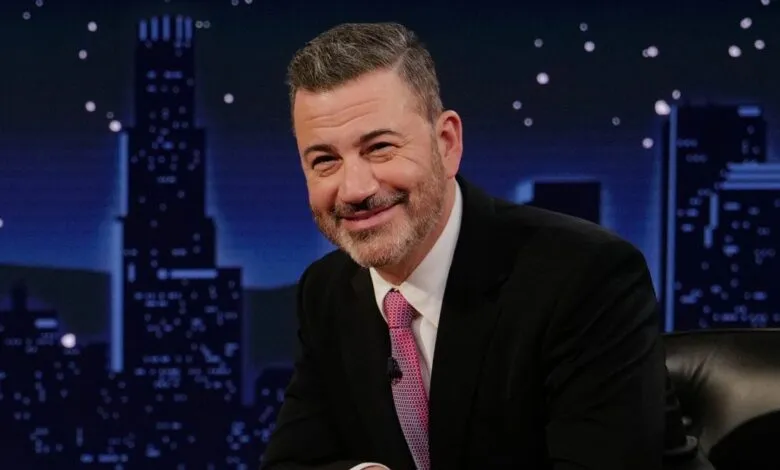 Jimmy Kimmel smiles in a suit against a city backdrop.