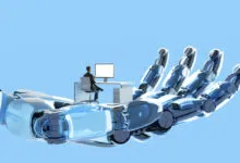 Robot hand gently supports a man working at his desk, symbolizing AI's role in the future of work.