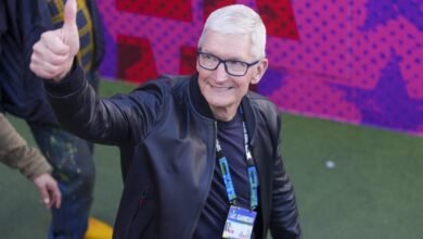 Tim Cook gives a thumbs up, wearing glasses and a black jacket.