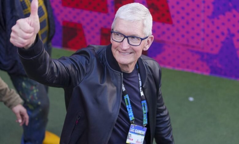 Tim Cook gives a thumbs up, wearing glasses and a black jacket.