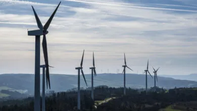 Wind farm with multiple turbines against a cloudy sky and rolling hills.