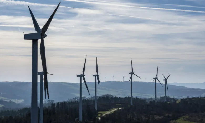 Wind farm with multiple turbines against a cloudy sky and rolling hills.