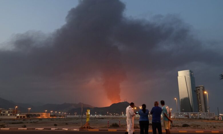People watch a large plume of smoke rising from an explosion in Fujairah.