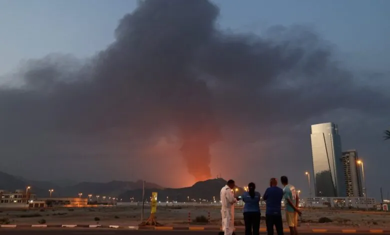 People watch a large plume of smoke rising from an explosion in Fujairah.