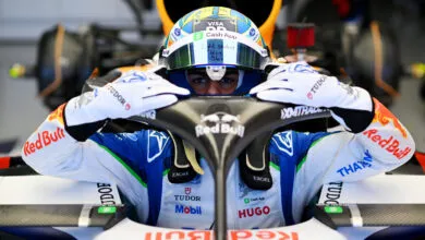 Arvid Lindblad in race car cockpit, wearing helmet and gloves, focused expression.