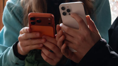 Two people holding smartphones, one orange, one white, close up.