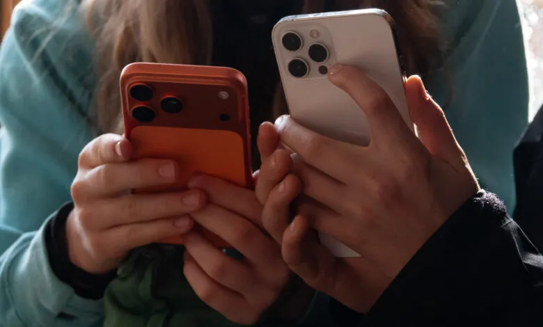 Two people holding smartphones, one orange, one white, close up.