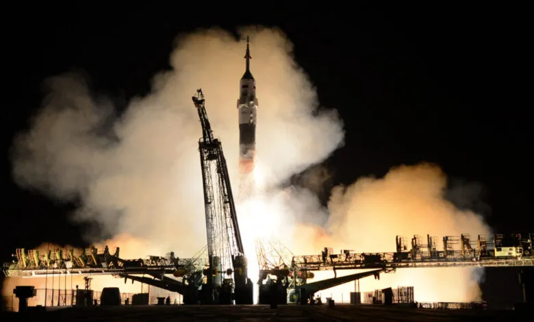 Soyuz rocket launches into the night sky amidst smoke and fire.