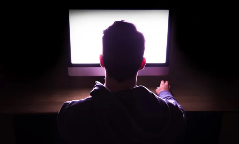 Person sits in dark room illuminated by a bright computer screen.