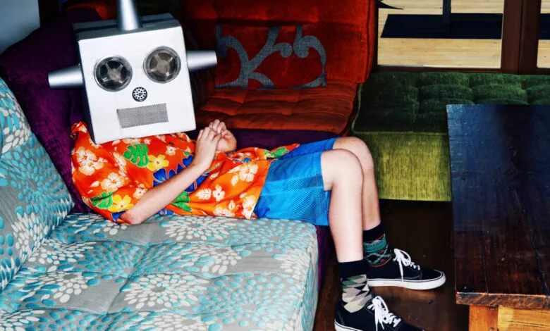 Person in robot mask and Hawaiian shirt lounges on colorful sofa.