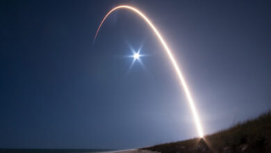 Long exposure shot of a rocket launch with a bright arc in the night sky.
