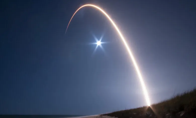 Long exposure shot of a rocket launch with a bright arc in the night sky.