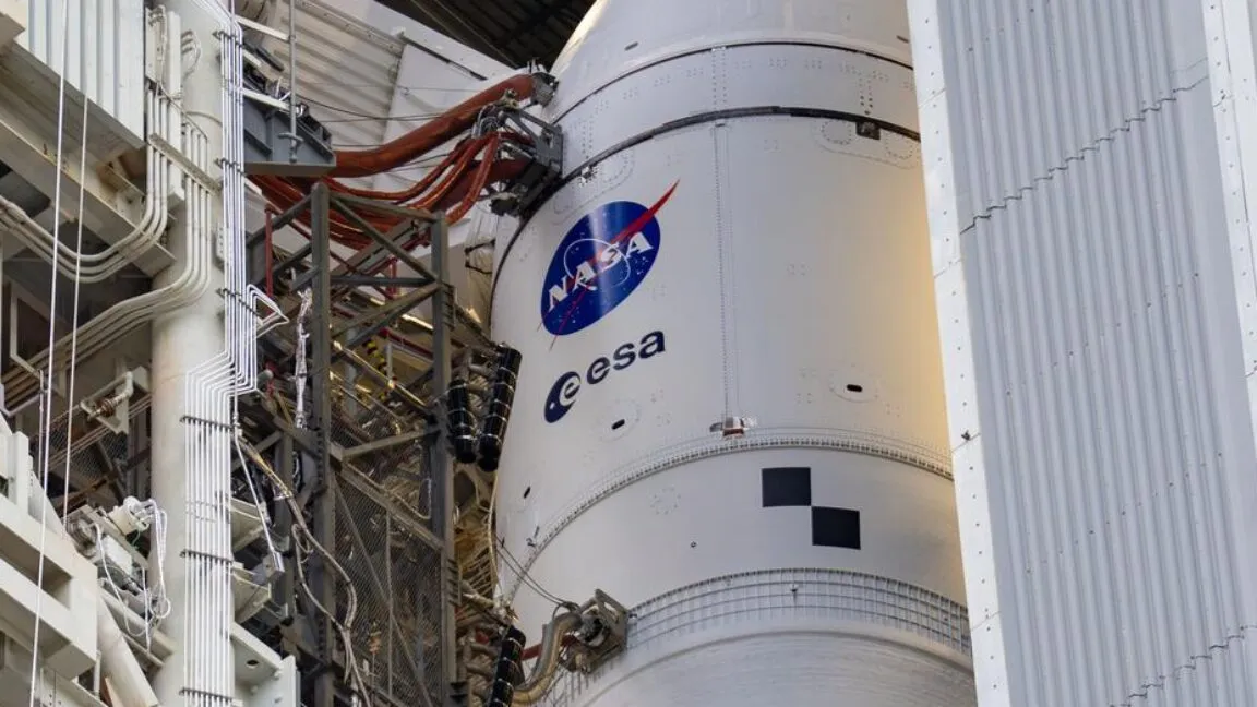 Close-up of a rocket with NASA and ESA logos, surrounded by scaffolding.
