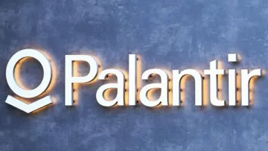 Palantir logo with white letters and orange glow on a gray textured wall.