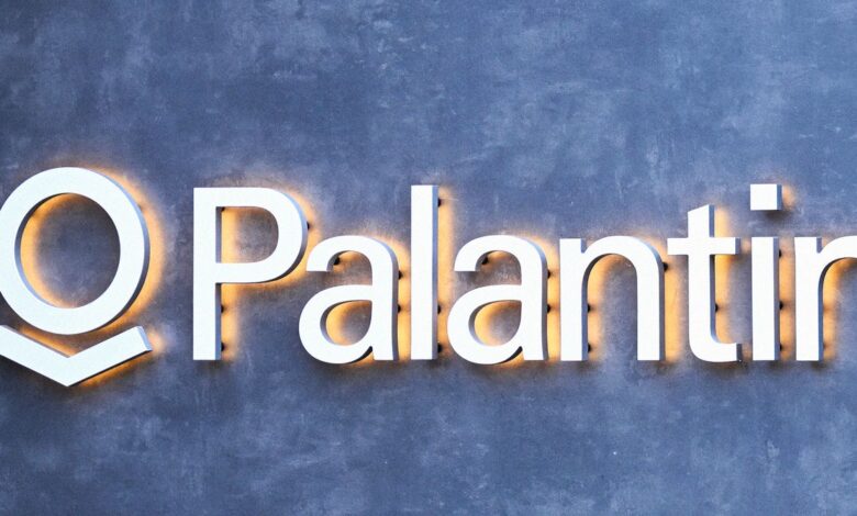 Palantir logo with white letters and orange glow on a gray textured wall.