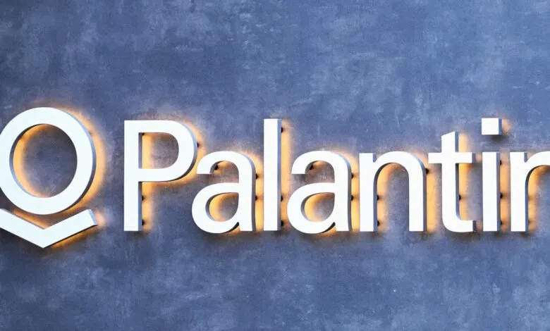 Palantir logo with white letters and orange glow on a gray textured wall.