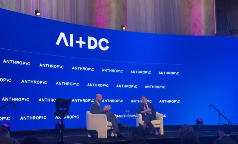Two men in suits sit on stage at AI+DC conference, audience in foreground.