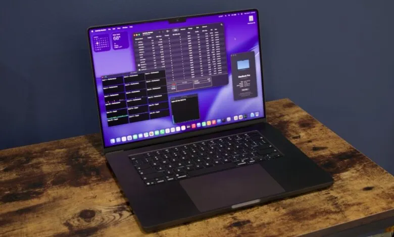 Open MacBook Pro on wooden desk displaying system performance metrics.