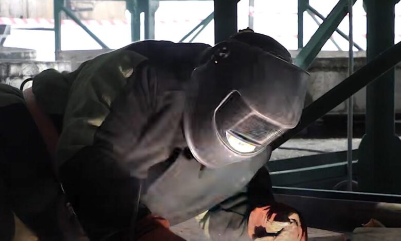 Welder in protective gear working on metal structure.