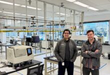 Two men stand in a modern, well-lit laboratory with scientific equipment.