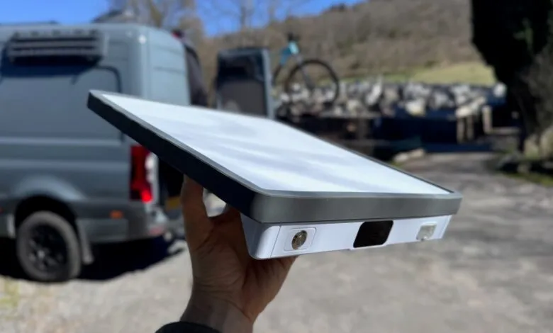 Hand holding a Starlink dish with a van and bike in the background.