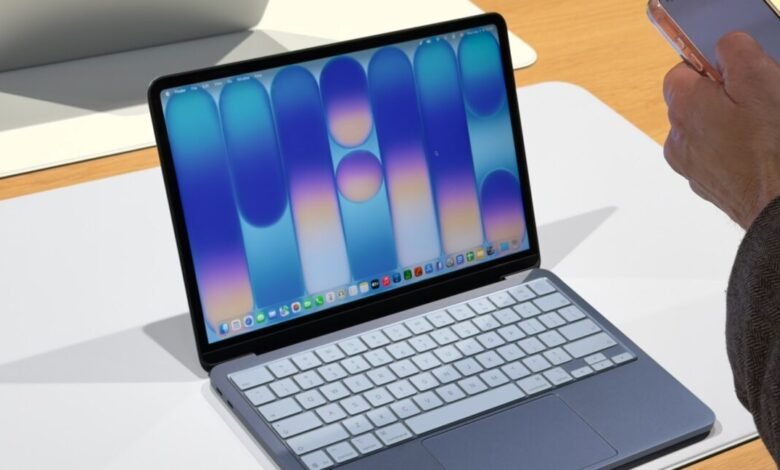 Laptop with blue wallpaper and a hand holding a smartphone.