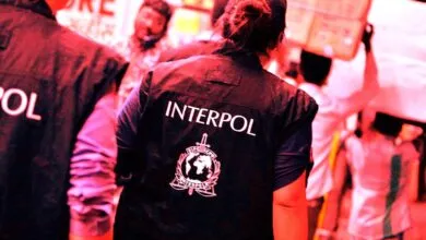 Interpol agents in vests with logo, surrounded by people.