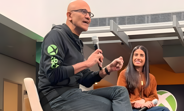 Satya Nadella speaking at an Xbox event with a woman smiling beside him.