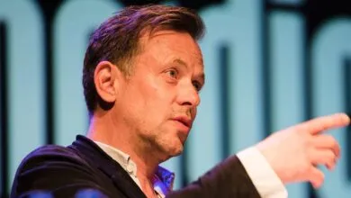 Man in suit pointing with serious expression on stage.