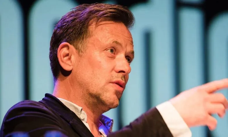 Man in suit pointing with serious expression on stage.