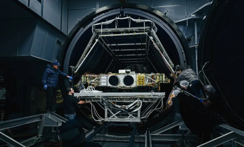 Technicians working on satellite inside a large thermal vacuum chamber.
