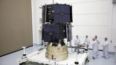 Satellite on platform with technicians in clean suits in a clean room.