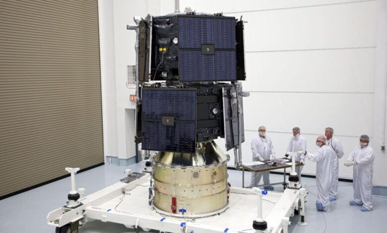 Satellite on platform with technicians in clean suits in a clean room.