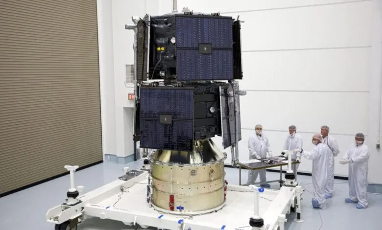 Satellite on platform with technicians in clean suits in a clean room.