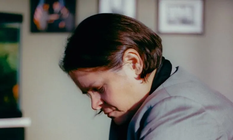 Woman in gray jacket looking down in an office setting.