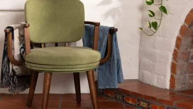 Green upholstered chair with wooden frame and blanket and jacket draped over arms.