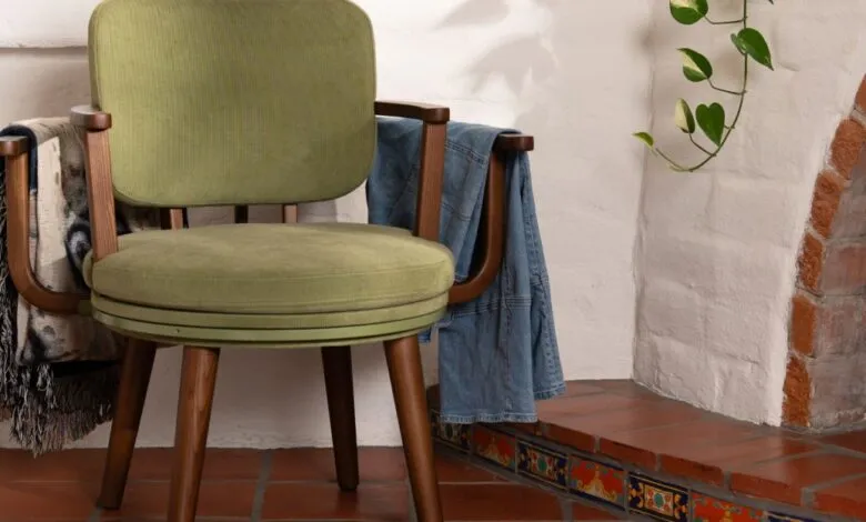 Green upholstered chair with wooden frame and blanket and jacket draped over arms.