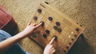 Person playing Tembo board game with wooden pieces on a textured carpet.