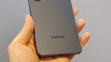Hand holding a gray Samsung smartphone, back view.