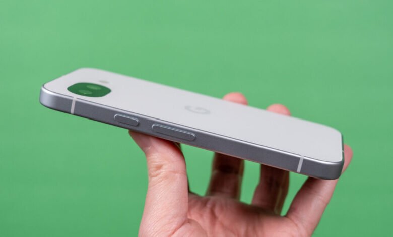 Hand holding a white and silver Google Pixel phone against green backdrop.