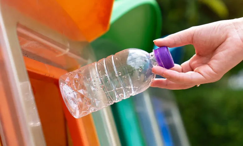 Hand placing plastic bottle into recycling bin with color-coded slots.